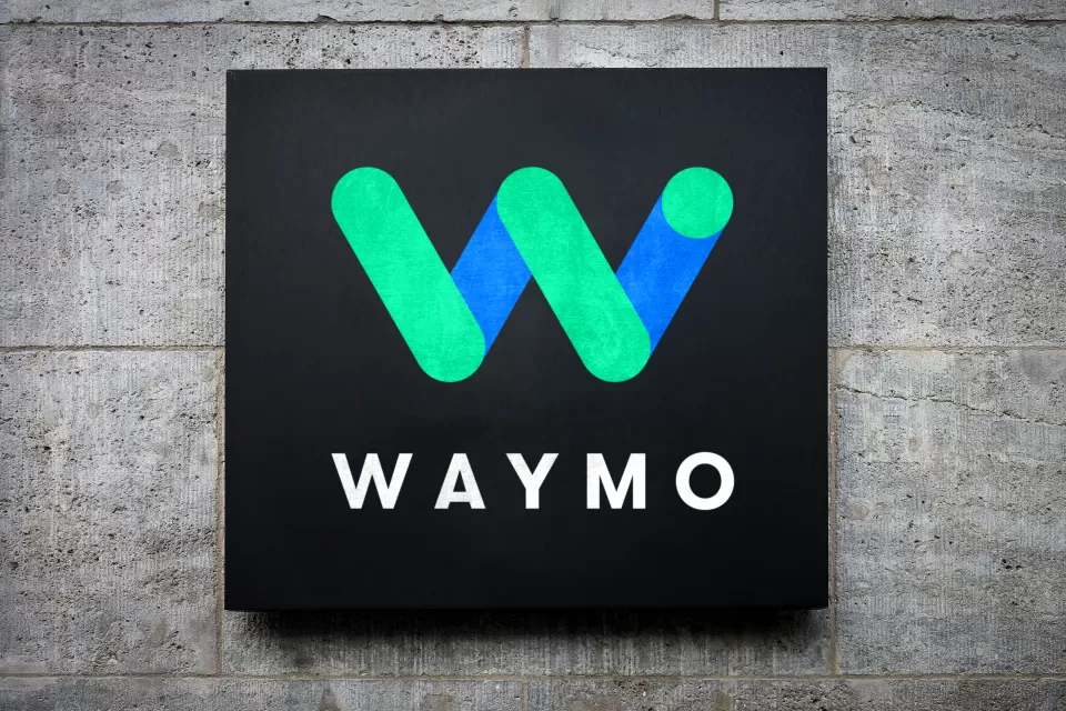 Blue and green Waymo logo on black square mounted on grey concrete background